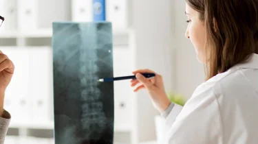 Læge og patient sidder og kigger på patientens røntgenbillede af hans rygsøjle.