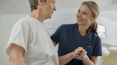 Sygeplejerske holder patient på skulder og smiler.