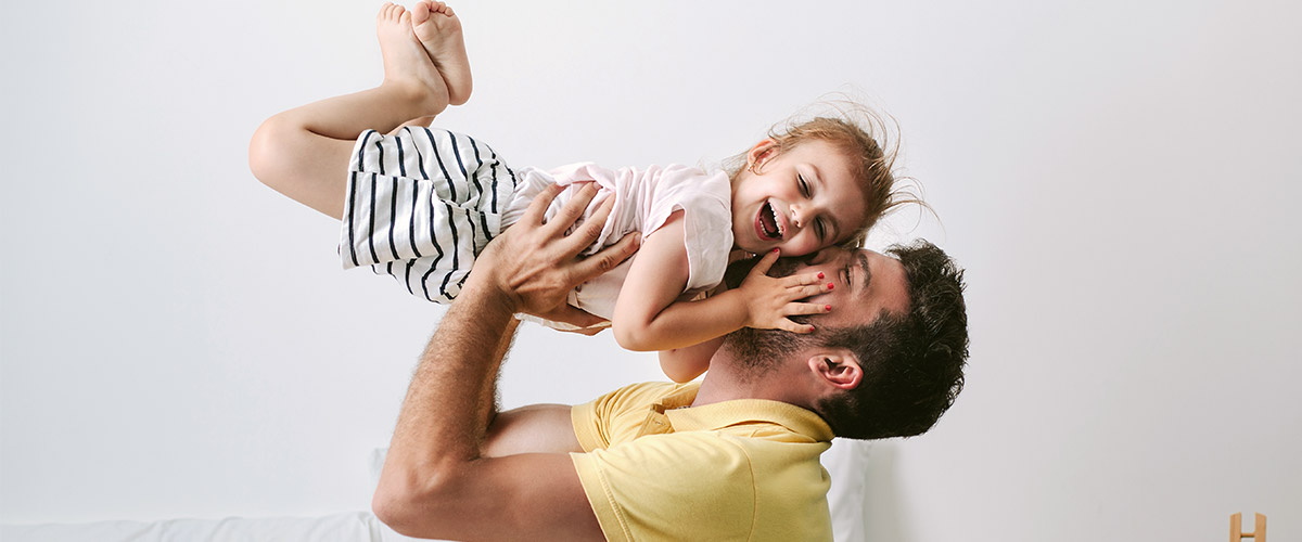 Far løfter sin grinende datter op i luften.