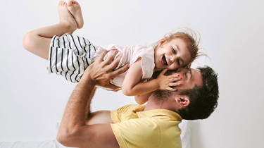 Far løfter sin grinende datter op i luften.