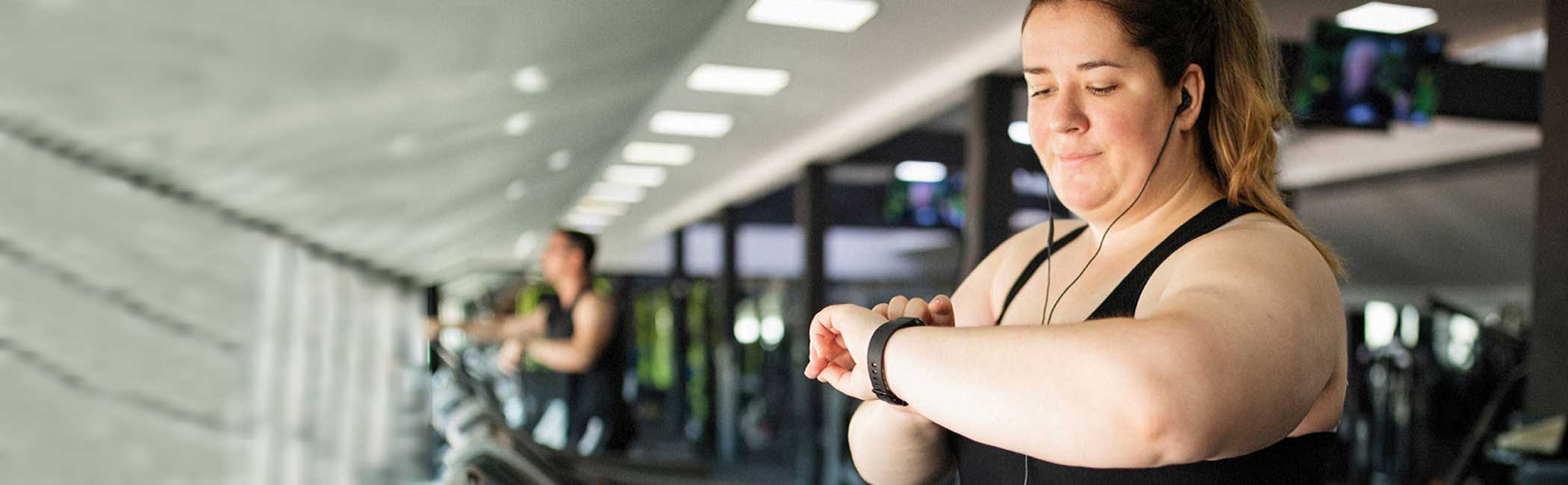 Overvægtig kvinde i fitnesscenter på løbebåndet.