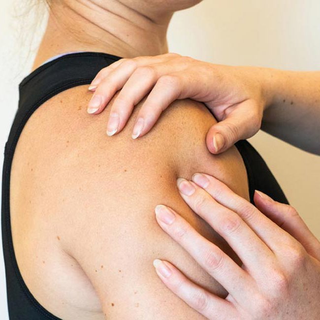 Fysioterapeut masserer patient på skulderen.