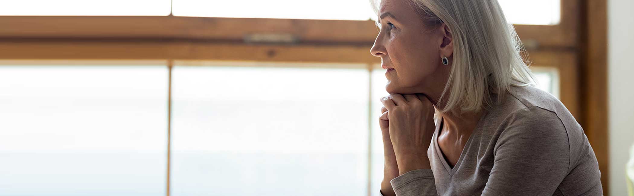 Kvinde sidder eftertænksomt og kigger ud i luften.