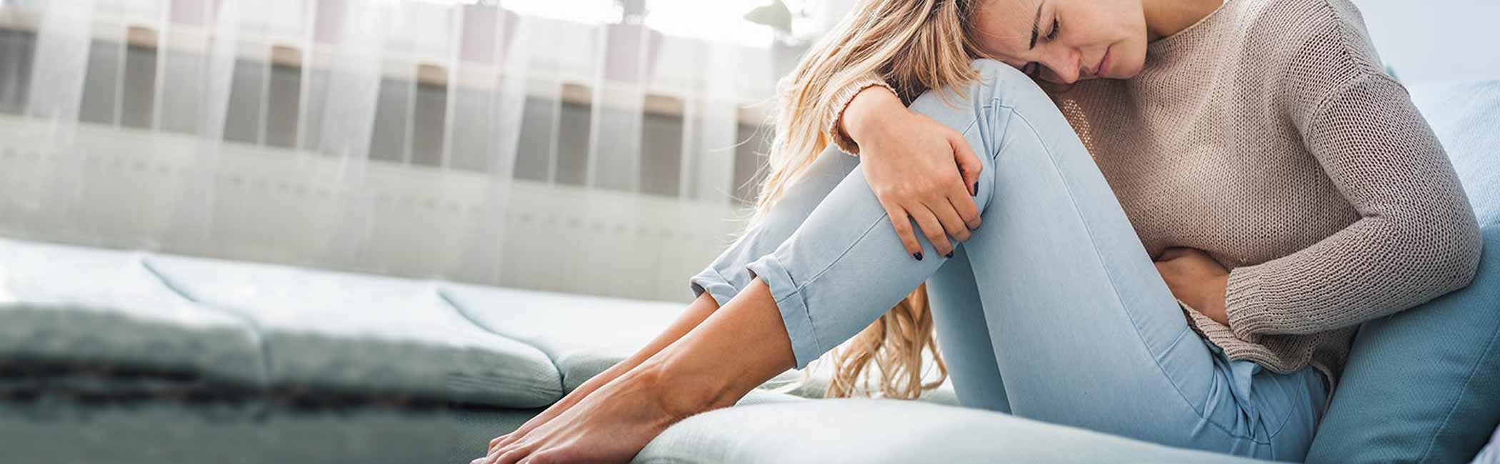 Kvinde sidder foroverbøjet med menstruationskramper.