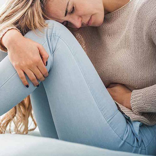 Kvinde sidder foroverbøjet med menstruationskramper.