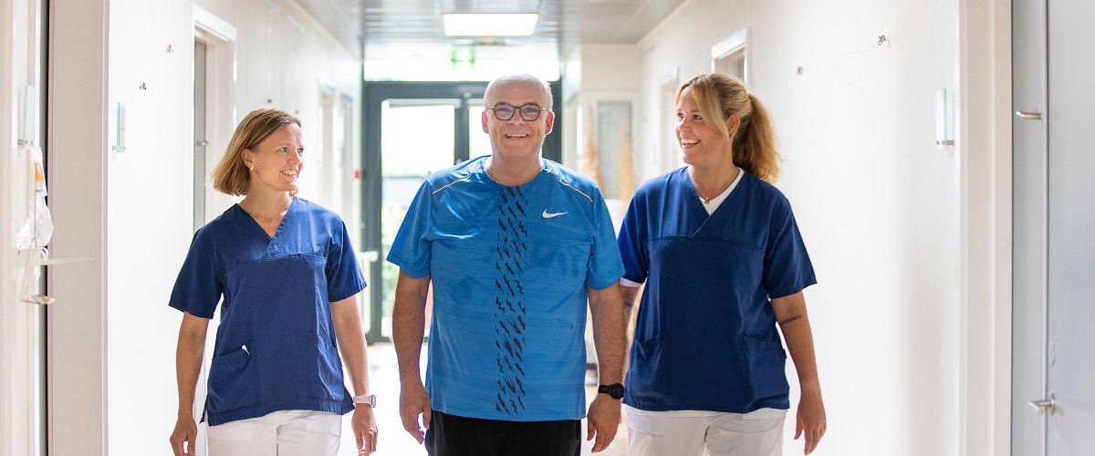 En patient kommer gående på gangen sammen med en læge og sygeplejerske.