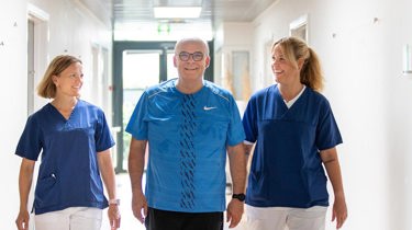 En patient kommer gående på gangen sammen med en læge og sygeplejerske.