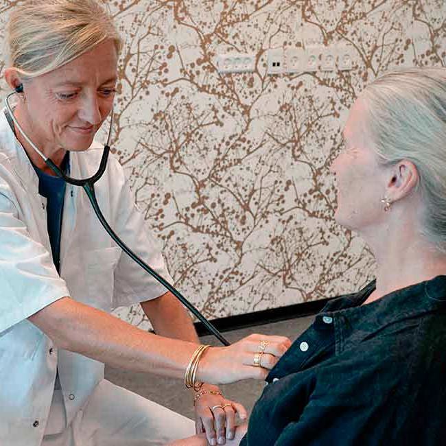 Helbredslæge lytter til hjertet på en patient.