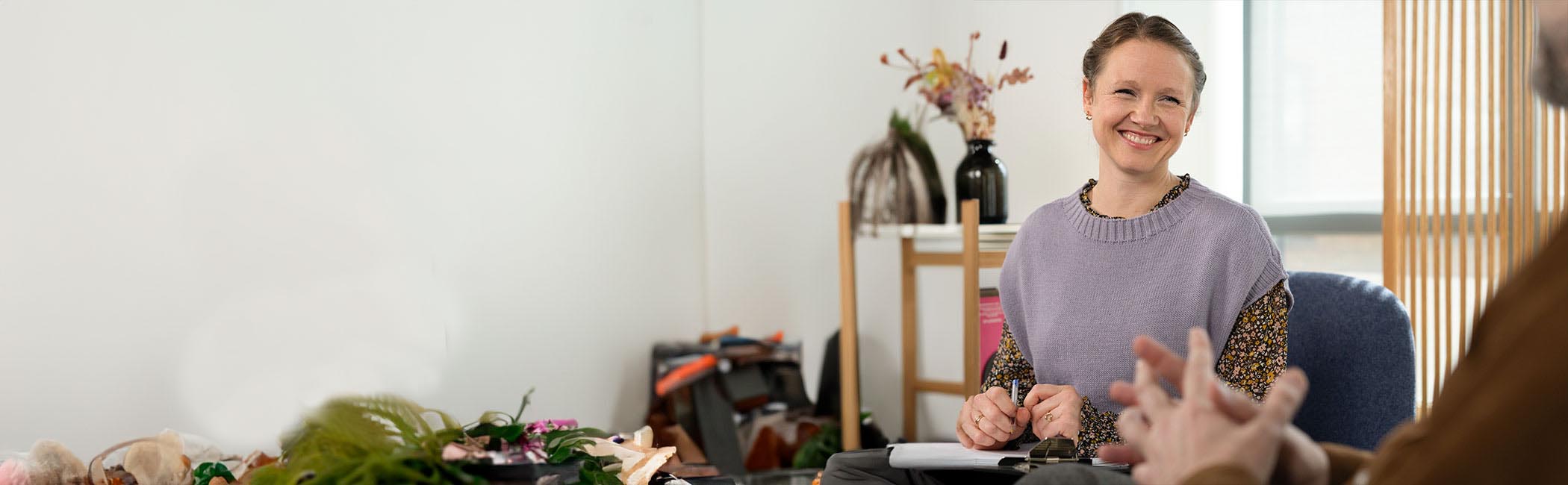 En kvinde sidder smilende og snakker med en mand.