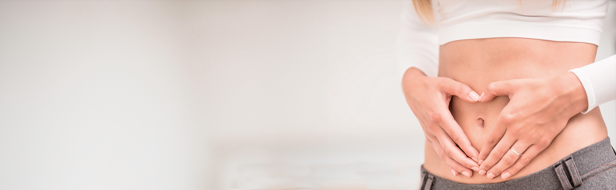 Kvinde danner et hjerte med sine hænder over maven.