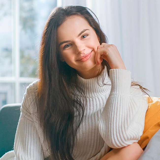 Glad kvinde sidder i sofa og smiler.