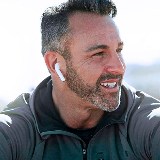 Glad mand sidder i naturen og lytter til musik.