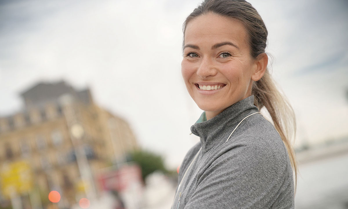 Kvinde i træningstøj smiler til kameraet.