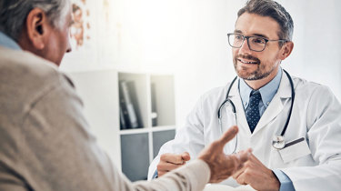 Mand sidder hos lægen og får forklaret mulige helbredsundersøgelser hos Aleris.