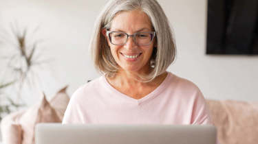 Kvinde sidder smilende ved sin computer.