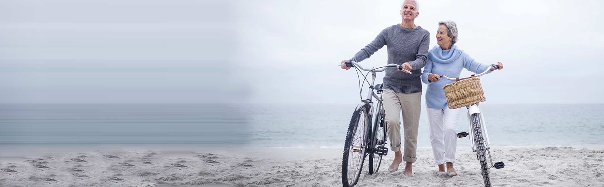 Ægtepar går med deres cykler på stranden.