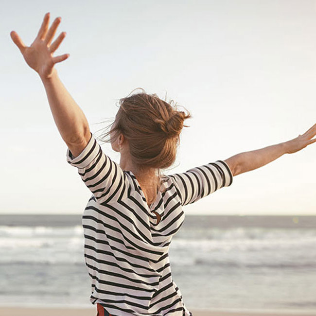 Kvinde strækker sig med armene i vejret på stranden.