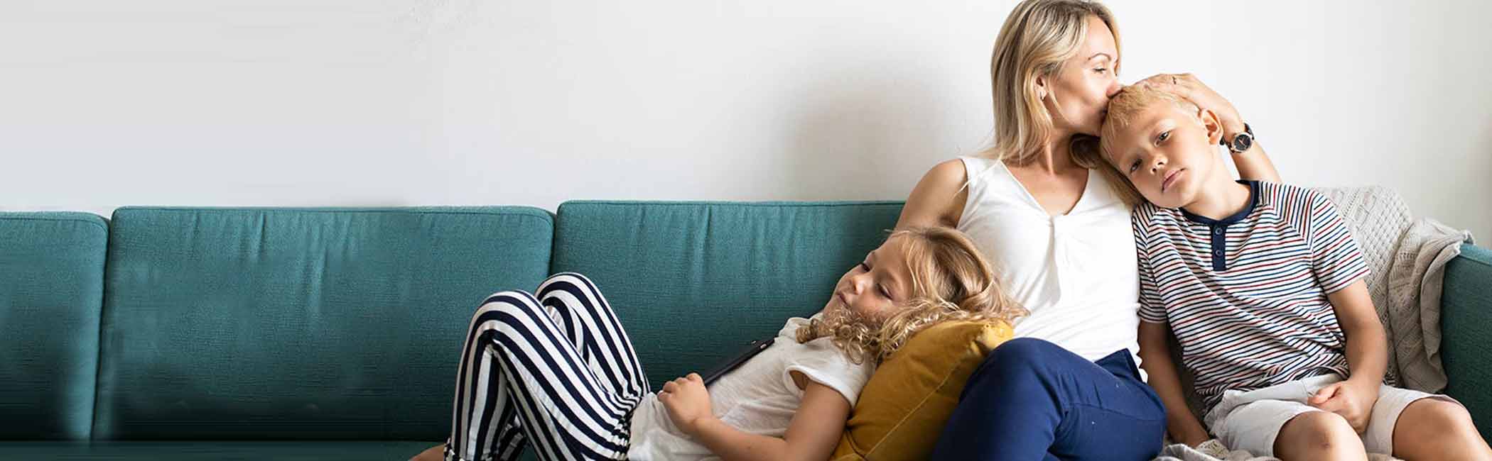 Mor sidder med sine to børn i sofaen.