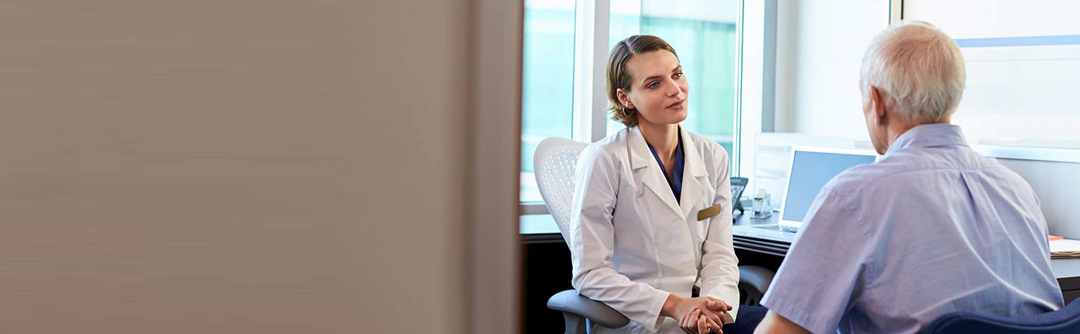 Læge og patient sidder og snakker om behandling af polypper på stemmebåndet.