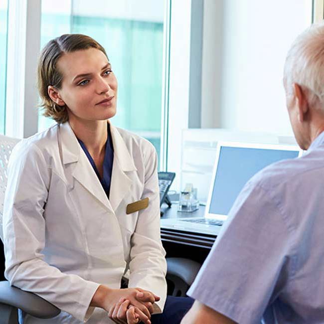 Læge og patient sidder og snakker om behandling af polypper på stemmebåndet.