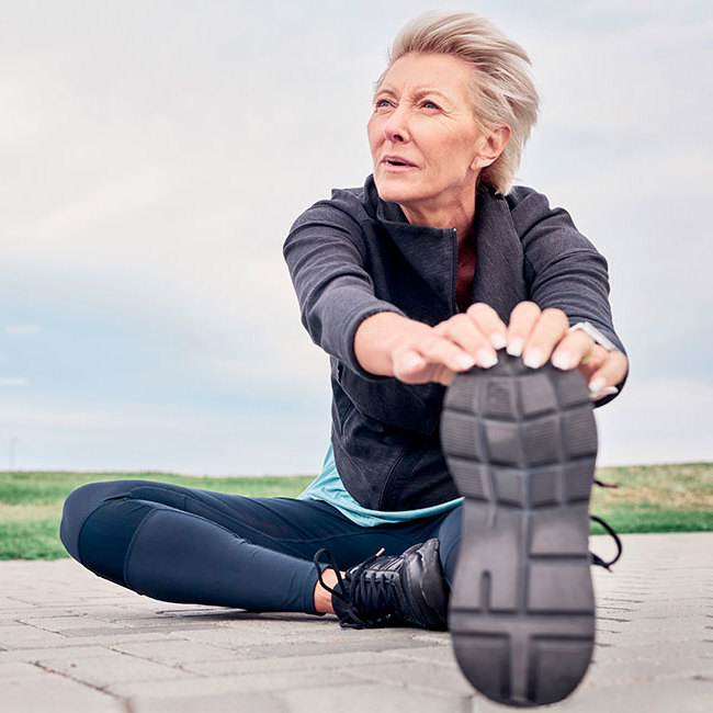 Kvinde sidder på jorden og strækker ud efter en løbetur.