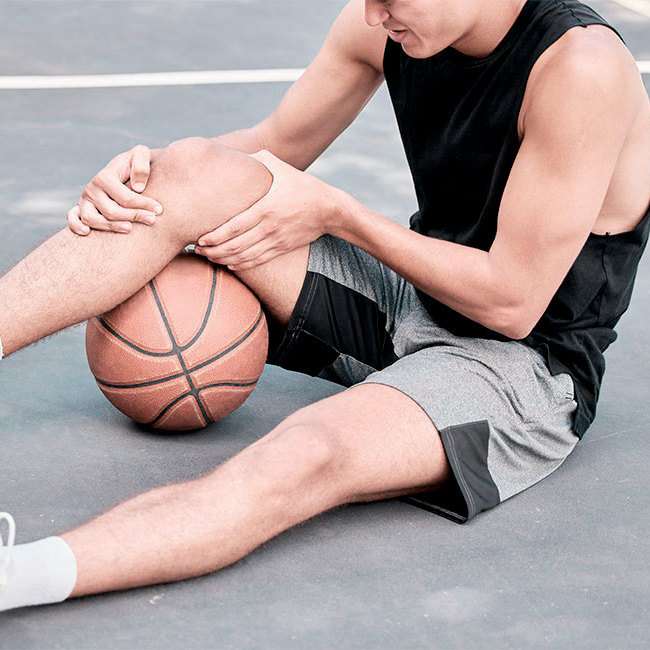 Basketballspiller sidder på jorden og holder på sit knæ.
