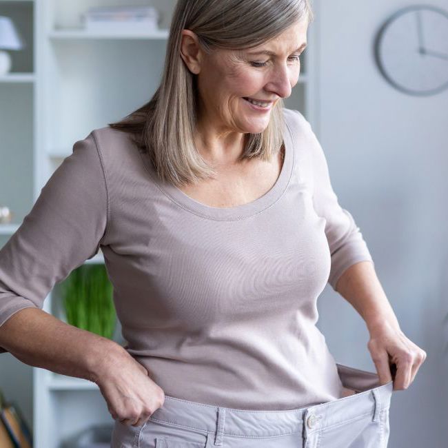 Glad ældre kvinde iført sine for store bukser, som passede inden hun fik lavet fedmeoperation ved Aleris.