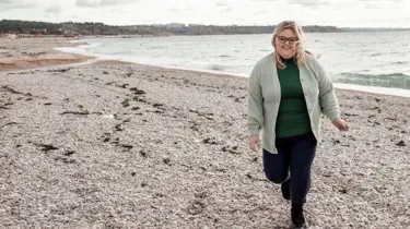 Overvægtig kvinde går på strand.