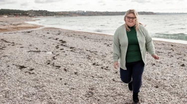 Overvægtig kvinde går på strand.