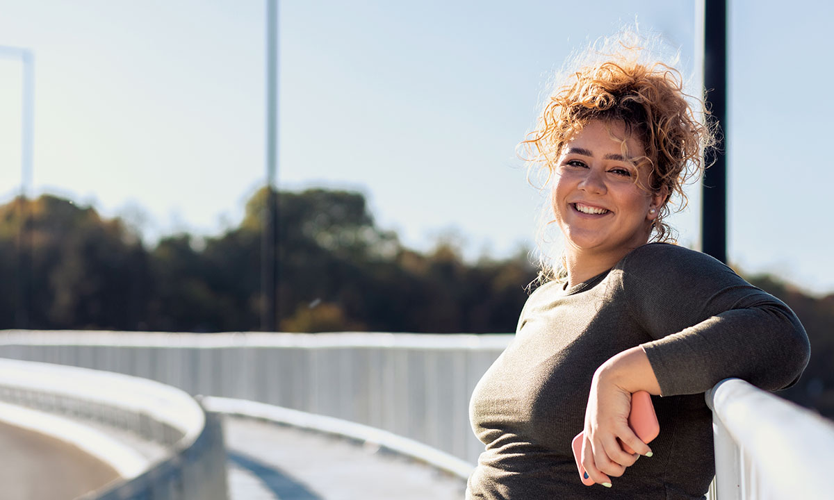 Kvinde står på en bro og smiler efter, at hun har motioneret.