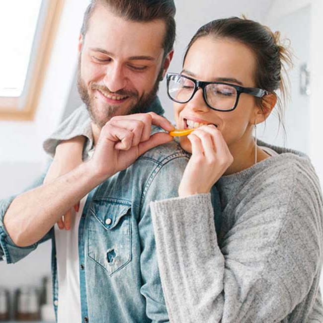 Glad mand og kvinde står i køkkenet og laver mad.