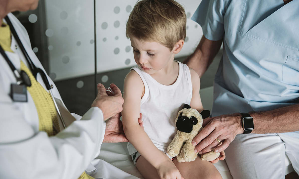 Et barn er ved at få en vaccination i trygge omgivelser og med sin bamse på skødet.