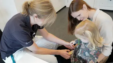 Sygeplejerske vaccinerer et barn, som sidder i sin mors favn.